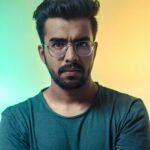 A thoughtful adult man with eyeglasses posing for a portrait with a vibrant backdrop.